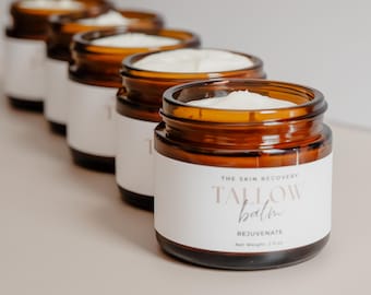 May include: Five amber glass jars of The Skin Recovery Tallow Balm Rejuvenate, a skin care product, with white labels. The jars are arranged in a row, with the closest jar in focus. The label on the closest jar reads "The Skin Recovery Tallow Balm Rejuvenate Net Weight 2 fl oz."