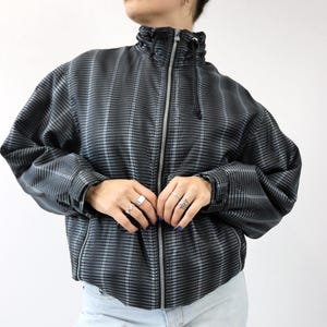 以下が含まれることがあります： 黒とグレーのチェック柄のジャケット。ハイカラーとフルレングスのジッパーが付いています。 ジャケットは長袖で、フィット感のあるデザインです。 薄いブルーのジーンズを履いています。