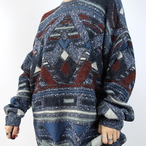 Pode incluir: Um suéter vintage oversized em tons de azul, bordô e branco. O suéter apresenta um padrão geométrico com formas de diamante e triângulo. As mangas compridas e o corte folgado criam um estilo descontraído. O suéter é feito de malha macia e texturizada.