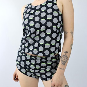 Könnte beinhalten: Ein zweiteiliges Set, bestehend aus einem schwarzen Tanktop und Shorts. Das Set ist mit einem Muster aus weißen, gestreiften Kreisen mit neongrünen Akzenten versehen. Das Tanktop hat einen Rundhalsausschnitt und die Shorts sind hoch tailliert.
