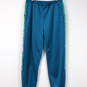 Puede incluir: Pantalones deportivos de color turquesa con cintura con cord&oacute;n y rayas laterales. Los pantalones tienen un patr&oacute;n geom&eacute;trico turquesa y morado en los laterales y un peque&ntilde;o logotipo de Fila. Los pantalones tienen cremalleras en los tobillos.