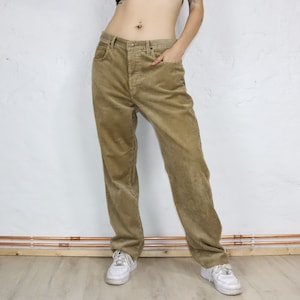 Könnte beinhalten: Eine hellbraune Cordhose. Die Hose hat einen geraden Schnitt und eine lockere Passform.