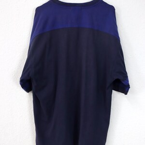 May include: A navy blue and dark blue color-blocked t-shirt hanging on a white hanger. The shirt has a crew neck and short sleeves. The top portion of the shirt is dark blue, and the bottom portion is navy blue.