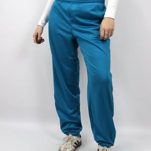 Puede incluir: Pantalones deportivos de color turquesa con cintura el&aacute;stica. Los pantalones tienen un corte holgado y se combinan con zapatillas blancas y beige. La tela parece lisa, posiblemente sint&eacute;tica.
