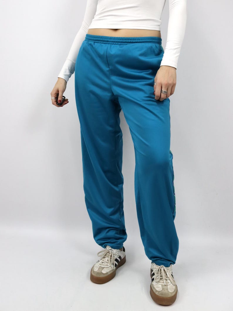 Puede incluir: Pantalones deportivos de color turquesa con cintura el&aacute;stica. Los pantalones tienen un corte holgado y se combinan con zapatillas blancas y beige. La tela parece lisa, posiblemente sint&eacute;tica.