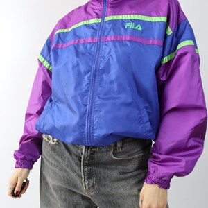May include: A vintage Fila track jacket in purple, blue, and green. The jacket has a high collar, a full zipper, and the Fila logo on the chest. The sleeves and waist are elasticized.