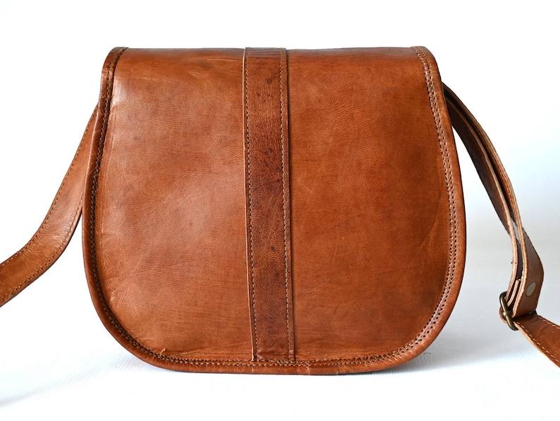 Handgefertigte Umhängetasche aus 100% Naturleder. Halbrunde From mit Druckschnallen-Verschluss in Vintage Optik. Tragriemen in der Länge verstellbar. Rückseite der Tasche vor weißem Hintergrund.
