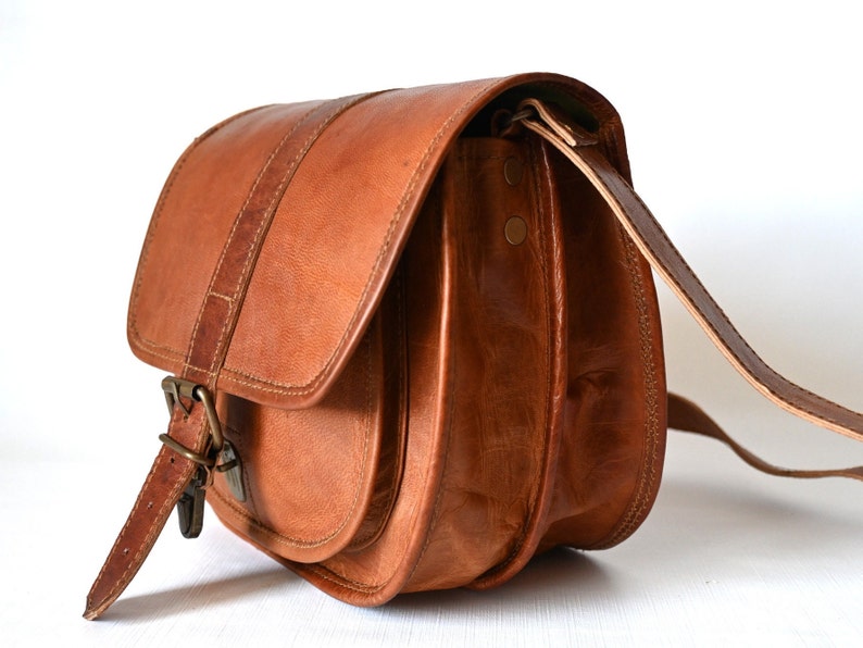 Handgefertigte Umhängetasche aus 100% Naturleder. Halbrunde From mit Druckschnallen-Verschluss in Vintage Optik. Tragriemen in der Länge verstellbar. Seitenansicht mit weißem Hintergrund.