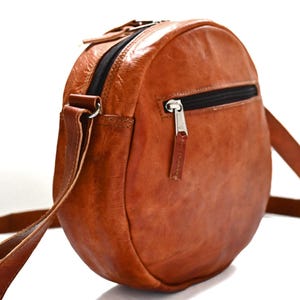 Handgenähte runde Tasche aus natürlich gegerbtem Leder. Trageriemen der Umhängetasche ist der Länge verstellbar. 
Seitenansicht der Tasche.