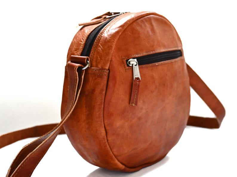Handgenähte runde Tasche aus natürlich gegerbtem Leder. Trageriemen der Umhängetasche ist der Länge verstellbar. 
Seitenansicht der Tasche.