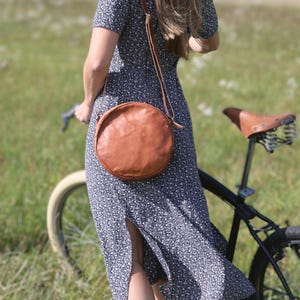Handgenähte runde Tasche aus natürlich gegerbtem Leder. Trageriemen der Umhängetasche ist der Länge verstellbar.
Tragebild an einem Model von Hinten.