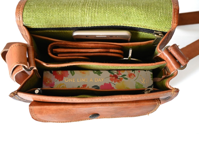 Handgefertigte Umhängetasche aus 100% Naturleder. Halbrunde From mit Druckschnallen-Verschluss in Vintage Optik. Tragriemen in der Länge verstellbar. Innenansicht der Tasche gefüllt mit Tagebuch, Geldbeutel, Handy und Sonnenbrille.