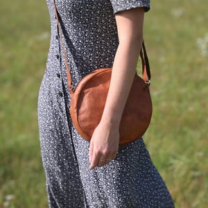 Handgenähte runde Tasche aus natürlich gegerbtem Leder. Trageriemen der Umhängetasche ist der Länge verstellbar. 
Seitenansicht der Tasche an einem Model.