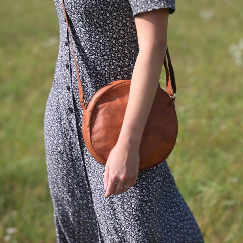 Handgenähte runde Tasche aus natürlich gegerbtem Leder. Trageriemen der Umhängetasche ist der Länge verstellbar. 
Seitenansicht der Tasche an einem Model.