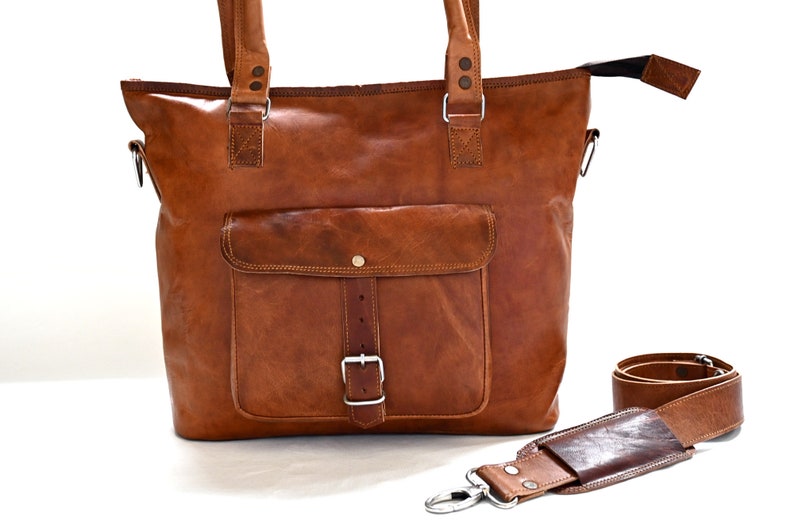 May include: A brown leather tote bag with a large front pocket and a buckle closure. The bag has a detachable shoulder strap.
