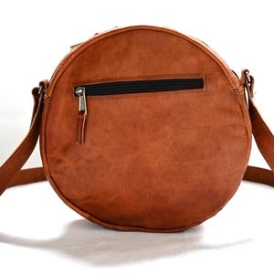 Handgenähte runde Tasche aus natürlich gegerbtem Leder. Trageriemen der Umhängetasche ist der Länge verstellbar. 
Frontansicht der Tasche.