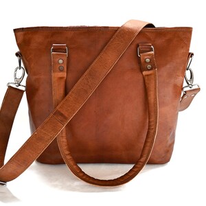 May include: A brown leather tote bag with a long adjustable shoulder strap. The bag has two top handles and a zip closure.