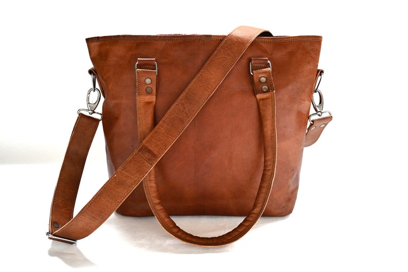 May include: A brown leather tote bag with a long adjustable shoulder strap. The bag has two top handles and a zip closure.
