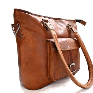 May include: A brown leather tote bag with a single front pocket and two top handles. The bag has a silver buckle on the front pocket and silver hardware on the handles.