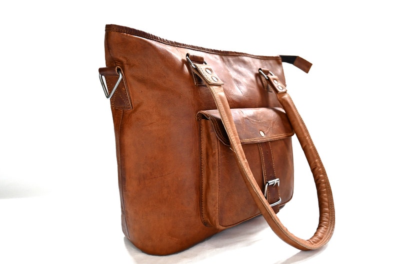 May include: A brown leather tote bag with a single front pocket and two top handles. The bag has a silver buckle on the front pocket and silver hardware on the handles.