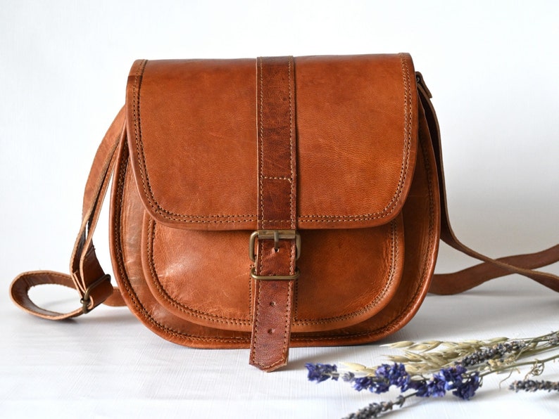 Handgefertigte Umhängetasche aus 100% Naturleder. Halbrunde From mit Druckschnallen-Verschluss in Vintage Optik. Tragriemen in der Länge verstellbar. Frontansicht mit weißem Hintergrund.