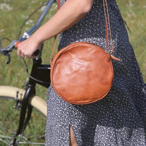 Handgenähte runde Tasche aus natürlich gegerbtem Leder. Trageriemen der Umhängetasche ist der Länge verstellbar.
Seitenansicht der Tasche an einem Model.