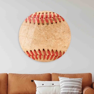 Puede incluir: Una pieza de arte mural redonda con forma de pelota de béisbol. La obra presenta una detallada representación de una pelota de béisbol, con costuras rojas sobre un fondo beige. Diseñada para montaje en pared.