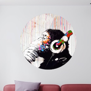 Puede incluir: Una calcomanía de pared circular que presenta una ilustración en blanco y negro de un mono con auriculares coloridos. El fondo es un lienzo blanco con líneas verticales de colores.