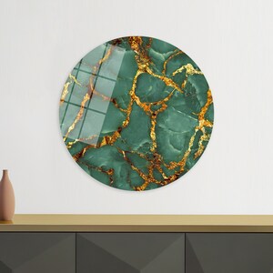 Op de afbeelding: Ronde wandkunst met een groen en gouden marmerontwerp. Het marmer heeft een draaiende structuur met gouden aderen.