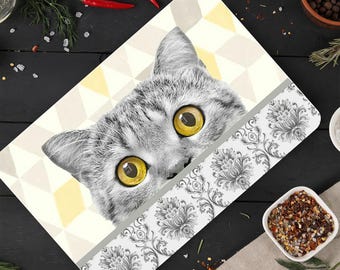 Peut inclure: Un chat gris et blanc regarde par-dessus un dessous-de-plat décoratif avec un motif géométrique et une bordure florale. Le chat a des yeux jaunes et une expression curieuse.