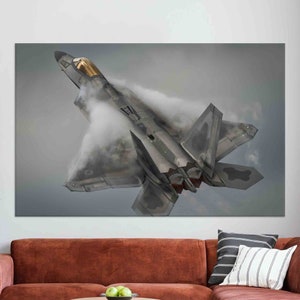 May include: A gray and black fighter jet with a gold canopy flies through the air, leaving a trail of white smoke behind it.