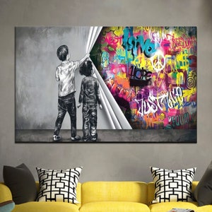 Puede incluir: Dos niños se paran frente a una pared gris, tirando de una sábana blanca para revelar un mural de graffiti colorido con palabras como "amor", "esperanza", "justicia" e "igualdad".