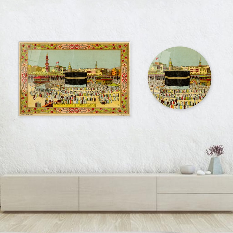 May include: Two framed prints depicting a religious scene with a central black structure, surrounded by a crowd of people. The rectangular print has a decorative border. The round print mirrors the scene. The prints are displayed on a white wall.