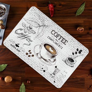Könnte beinhalten: Weißer und schwarzer Untersetzer zum Thema Kaffee mit Ziegelhintergrund. Der Untersetzer zeigt eine Tasse Kaffee, Kaffeebohnen und den Text "Coffee, I'd rather take compliments".