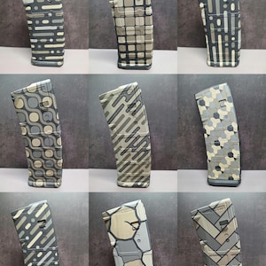 May include: A collection of nine rifle magazines, each featuring a distinct geometric pattern in shades of tan, gray, and black. The designs include grids, hexagons, herringbone, and abstract lines, all displayed in a grid layout.