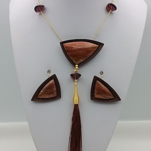 May include: A brown and gold necklace with a triangular pendant and matching earrings. The pendant has a tassel.