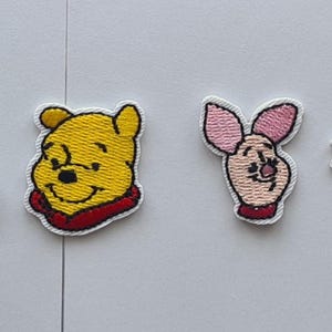 May include: A selection of embroidered patches featuring characters from a well-known children's series. The patches include a yellow bear in different poses, a donkey, a pig, and a tiger. The patches are brightly coloured and have a white border.