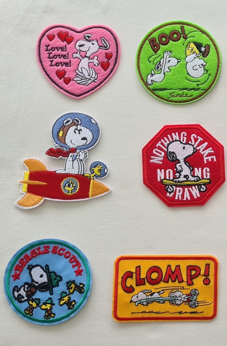 May include: Six embroidered iron-on patches featuring the Peanuts characters, including Snoopy. The patches feature various themes, including love, sports, and space exploration. The patches are colorful and feature a variety of designs.