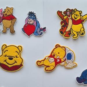May include: A selection of embroidered Winnie the Pooh character patches. The patches show Pooh, Piglet, Eeyore, and Tigger in different poses, with bright colours and detailed stitching. These patches are suitable for decorating clothing or accessories.