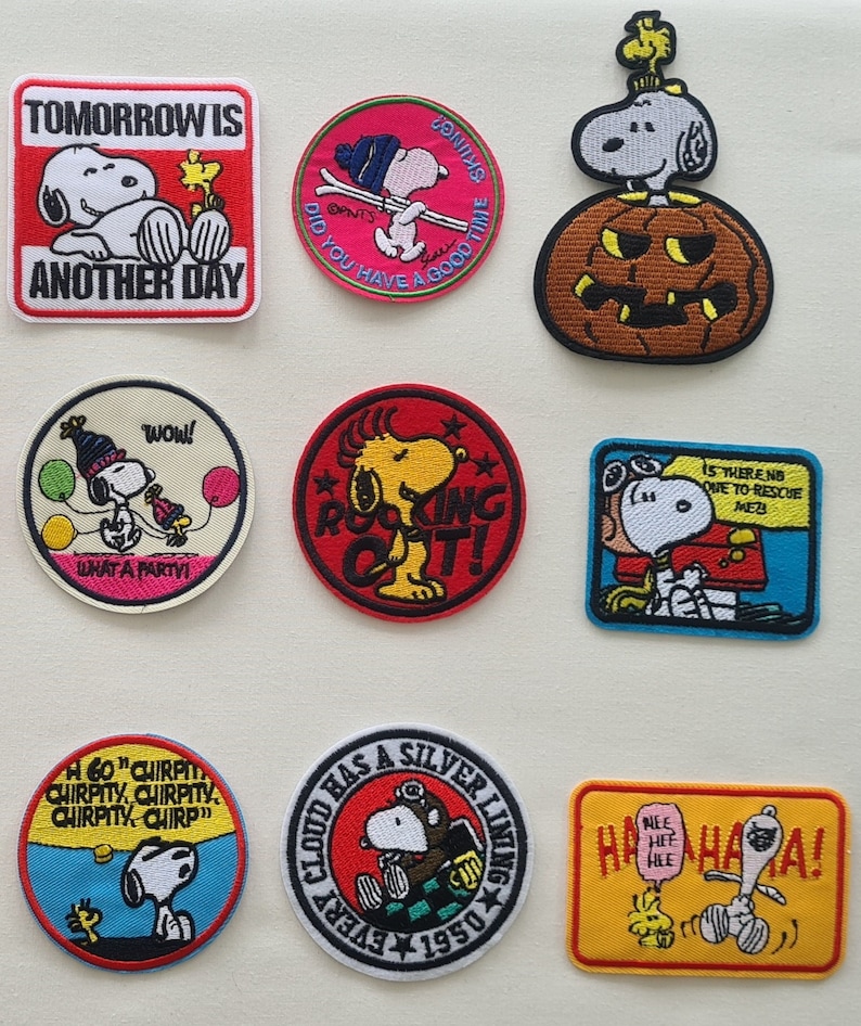 May include: Nine embroidered iron-on patches featuring the Peanuts character Snoopy. The patches are colorful and feature various scenes and sayings, including "Tomorrow is another day", "Did you have a good time skiing?", "What a party!", "Rocking out!", "Is there no one to rescue me?", "60" chirpity, chirpity, chirpity, chirp", "Every cloud has a silver lining 1950", and "Nee hee hee haha!"