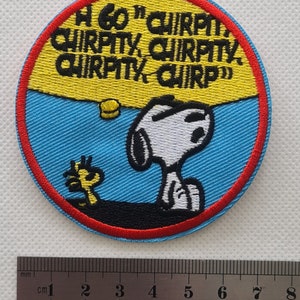 May include: A round, blue and yellow embroidered patch featuring Snoopy and Woodstock. The text on the patch reads "A60' CHIRPO CHIRPITY, CHIRPITY, CHIRPITY CHIRP".