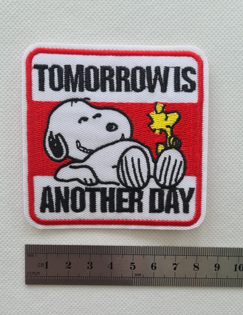 May include: White embroidered patch with a red border featuring a cartoon dog with a yellow bird. The text "TOMORROW IS ANOTHER DAY" is written in black.