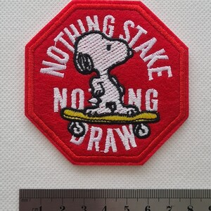 May include: Red octagonal embroidered patch with white stitching. The patch features a cartoon dog skateboarding with the text "Nothing Stake Nothing Draw".