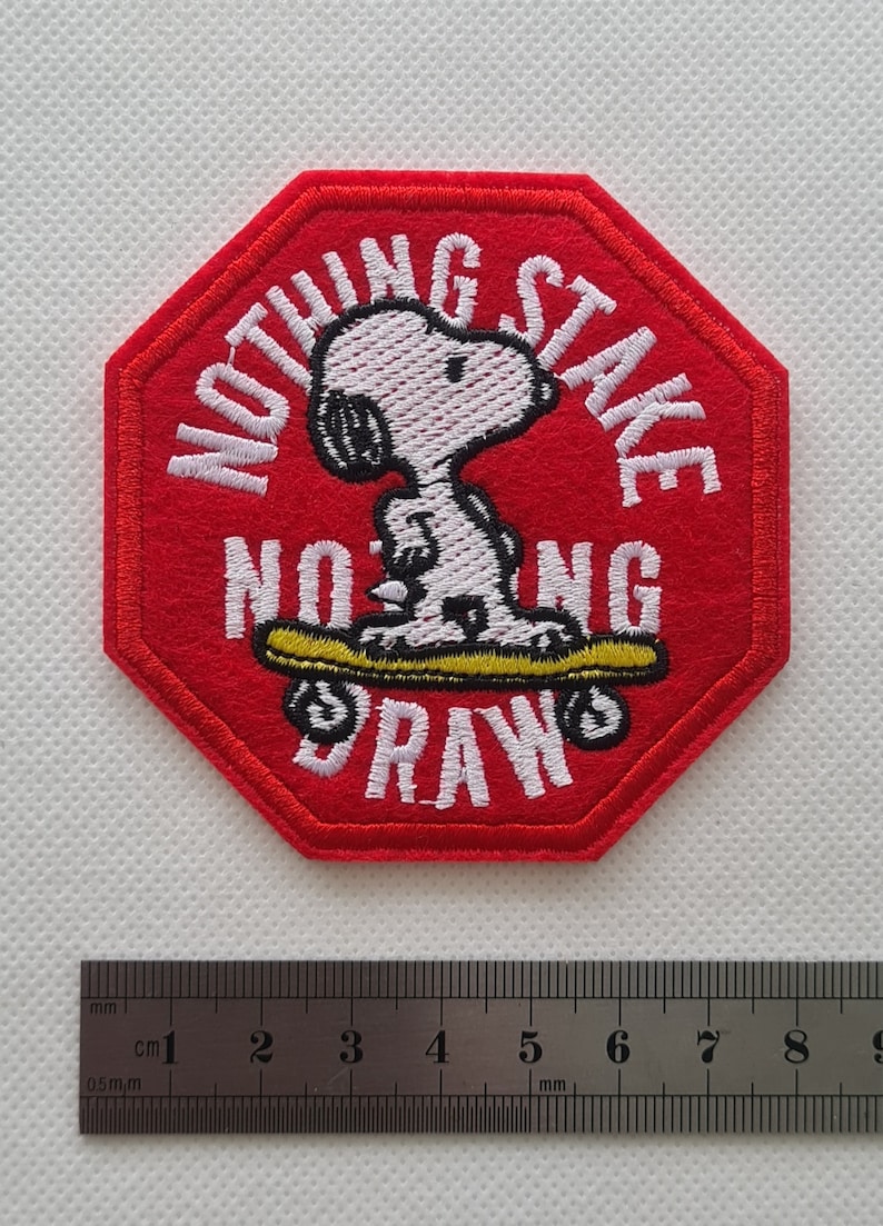 May include: Red octagonal embroidered patch with white stitching. The patch features a cartoon dog skateboarding with the text "Nothing Stake Nothing Draw".