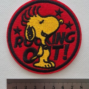 May include: Red, white, and yellow embroidered iron-on patch featuring a cartoon dog with the text "Rockin' Out!"