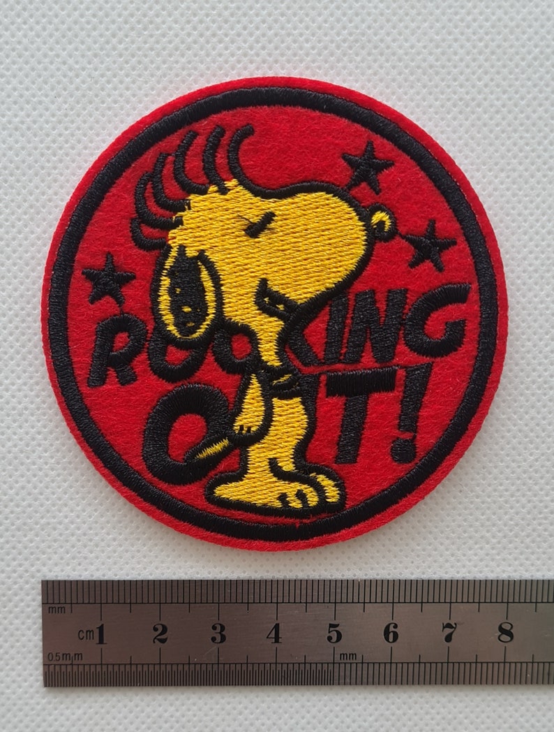 May include: Red, white, and yellow embroidered iron-on patch featuring a cartoon dog with the text "Rockin' Out!"