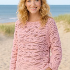 Könnte beinhalten: Ein hellrosa Langarmpullover mit einem komplizierten Ajour-Strickmuster mit wiederkehrendem Blumenmotiv, einem Rundhalsausschnitt und einem geraden Saum. Das Kleidungsstück ist mit einer zarten, luftigen Textur an Körper und Ärmeln gefertigt.