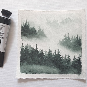 May include: A watercolor painting of a forest landscape in shades of green and gray. The painting is next to a tube of "Perylene Green" watercolor paint. The paint tube is black with white text and a black cap. The painting depicts a misty forest scene.