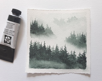 May include: A watercolor painting of a forest landscape in shades of green and gray. The painting is next to a tube of "Perylene Green" watercolor paint. The paint tube is black with white text and a black cap. The painting depicts a misty forest scene.