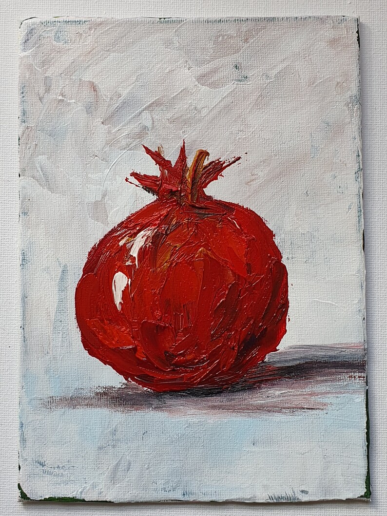 May include: A vibrant oil painting of a pomegranate. The fruit is a deep red with textured brushstrokes, set against a white and light blue background. The painting captures the pomegranate's shape and details, with a focus on the fruit's rich color.